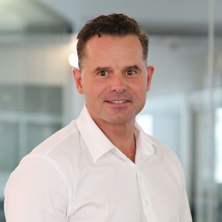 Martin Bosshardt smiling at the camera, standing in an office setting with glass walls and blurred background.