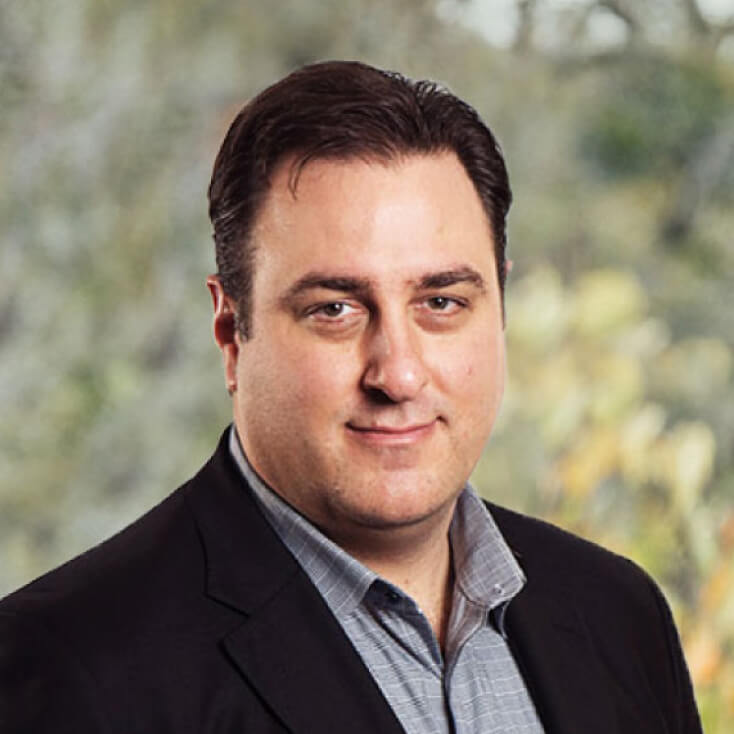 Michael Fey standing in front of a blurred natural background, featuring soft green and yellow tones.