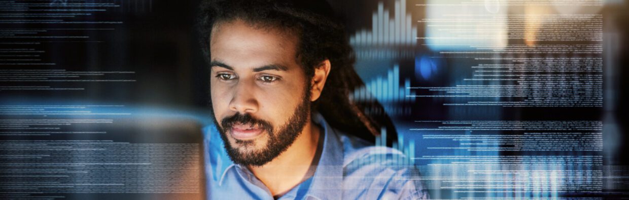 A man with dreadlocks focused on a laptop screen, surrounded by digital coding and data visuals. The setting is dimly lit, highlighting the screen's glow.