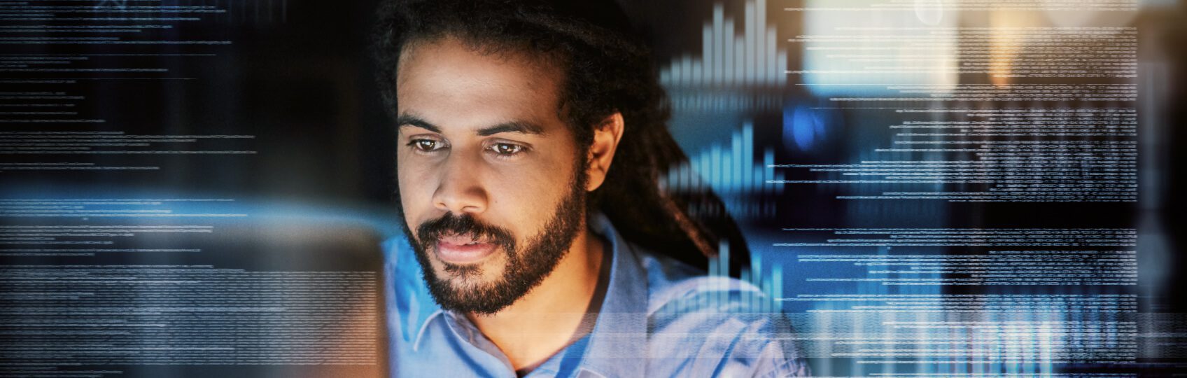A man with dreadlocks focused on a laptop screen, surrounded by digital coding and data visuals. The setting is dimly lit, highlighting the screen's glow.