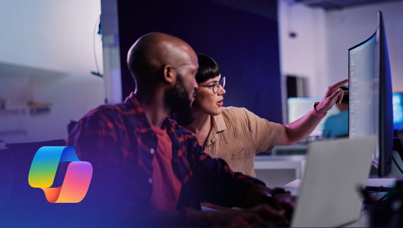 A man and a woman collaborating at a computer workstation, discussing work on the screen. The setting is modern and well-lit, with screens displaying programming or digital content. The image includes a logo on the bottom left corner, relevant to Microsoft Copilot for security.