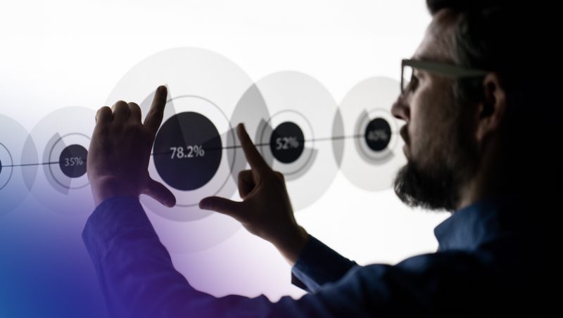 A person with glasses interacting with a digital interface displaying percentages, such as 35%, 52%, and 78.2%, in a modern, minimalistic setting.