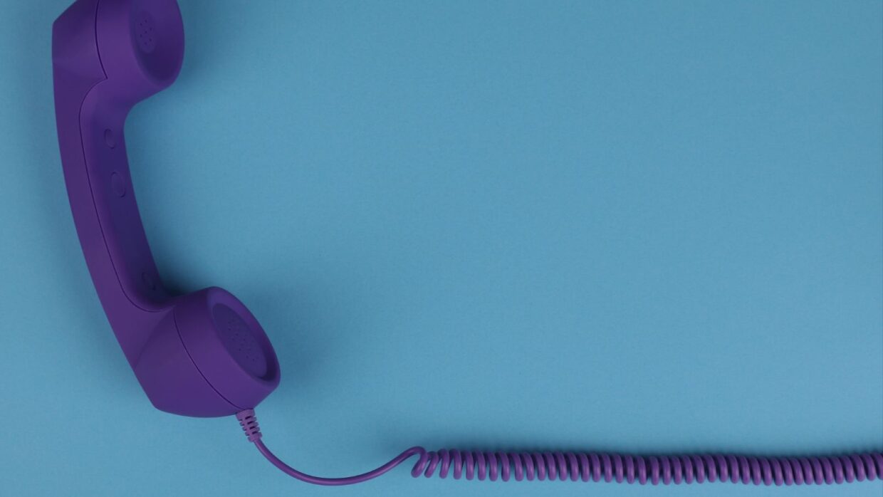 A purple telephone handset with a curly cord lying on a turquoise background.