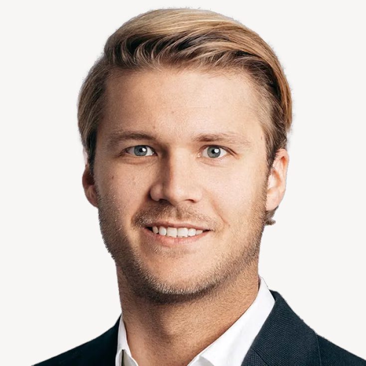 Christian Küpper, wearing a black suit jacket over a white shirt, against a plain white background.