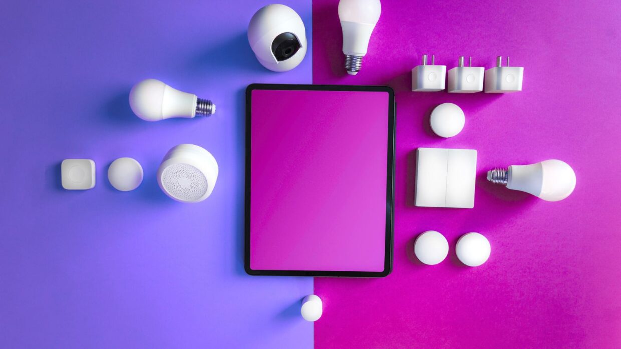 A flat lay arrangement of smart home devices on a purple and pink background, including an electronic tablet, smart bulbs, sensors, and plugs, illustrating IoT and OT security applications.