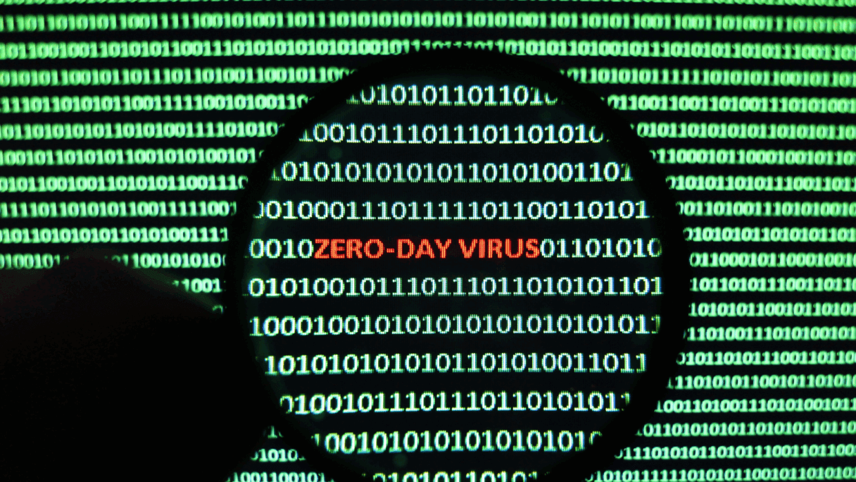 Close-up view of a computer screen displaying binary code, with the phrase "ZERO-DAY VIRUS" highlighted in red within a circular frame.