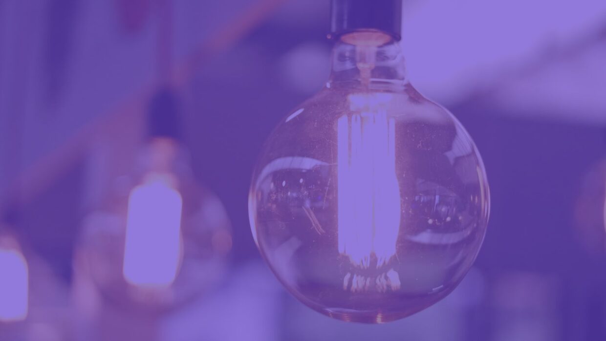 A close-up of a glowing light bulb with a warm filament, surrounded by other bulbs blurred in the background. The scene is illuminated with a purple hue, creating a modern ambiance.