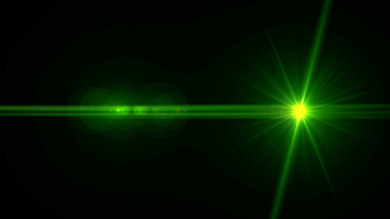A green laser beam with a bright star-like point of light in the center, set against a black background. The beam is surrounded by a faint glow and light flares, creating a dynamic visual effect.