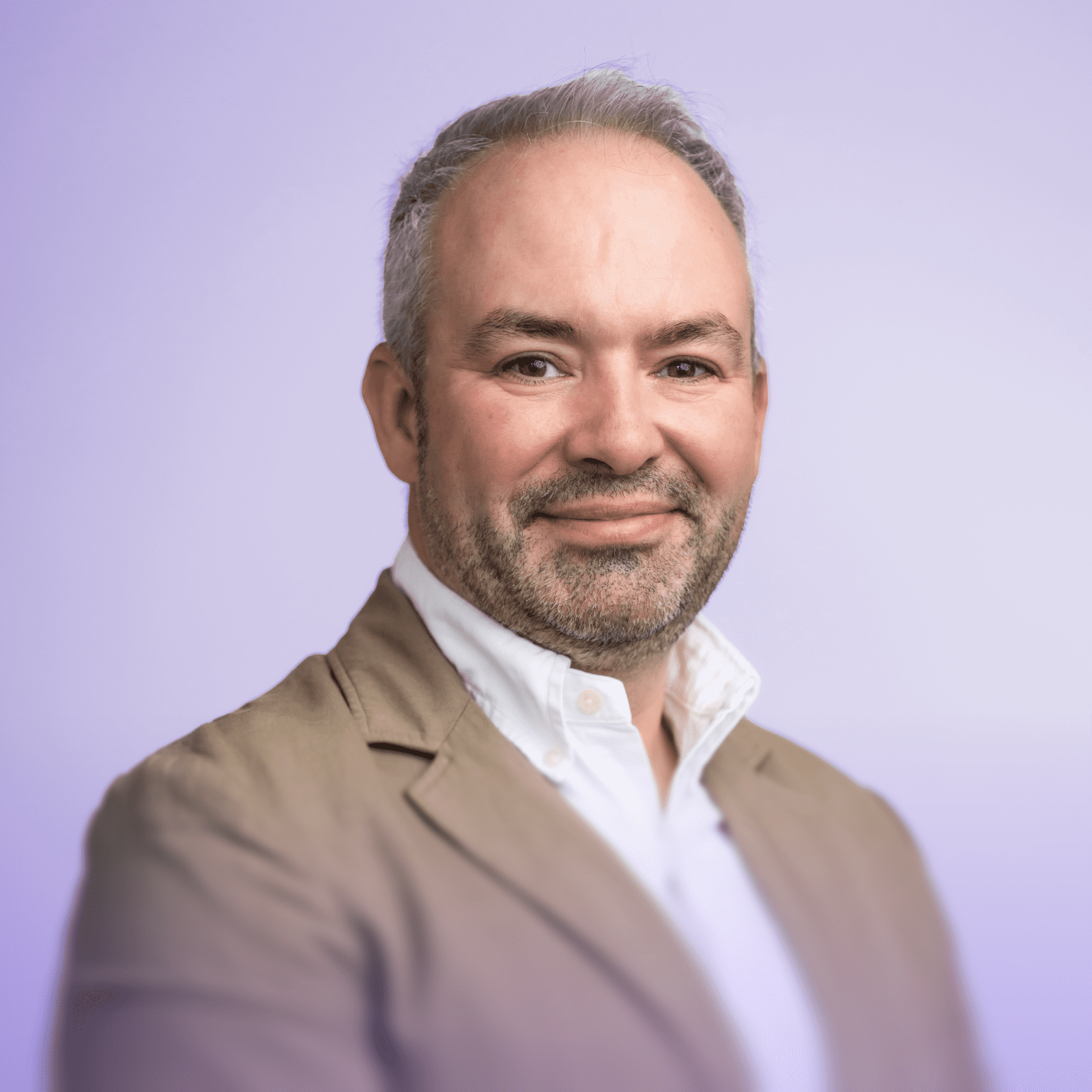 Craig Jones wearing a light blue button-up shirt stands smiling in a modern office environment.