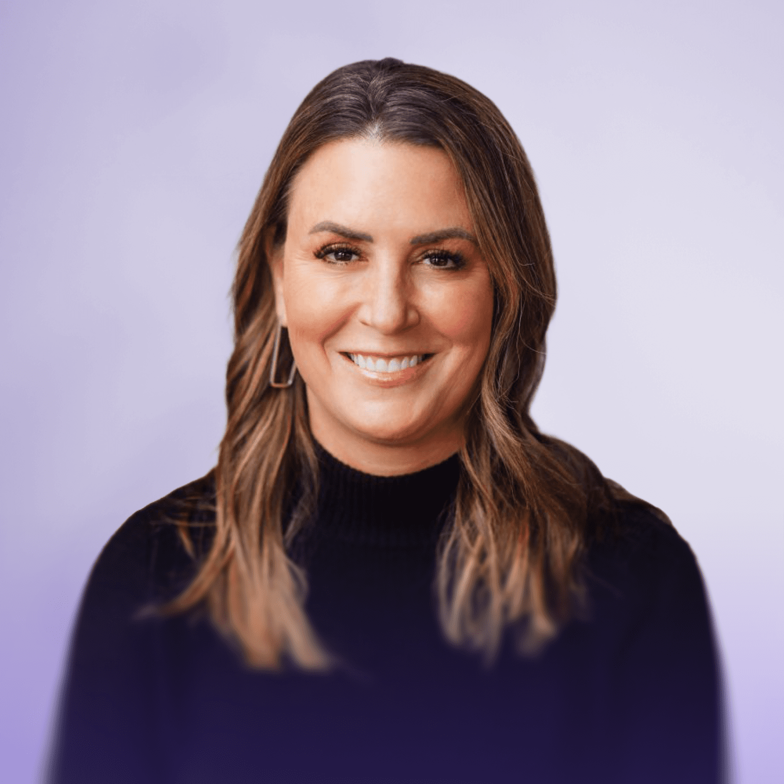 Karen Brooks wearing a black turtleneck sweater smiles at the camera. She is seated on a green couch, with a neutral background.