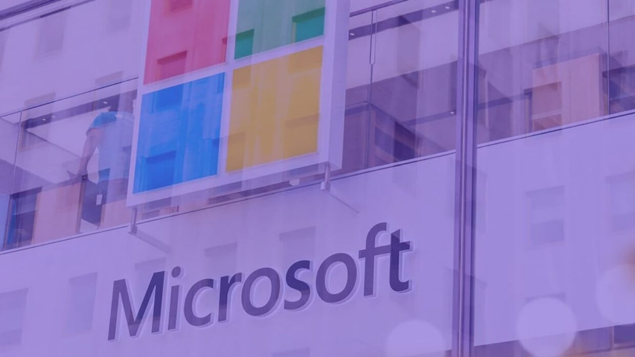 The Microsoft logo displayed prominently on a building exterior. The logo features a four-pane colored design with red, green, blue, and yellow squares above the word "Microsoft" in bold lettering. The image has a purple tint.