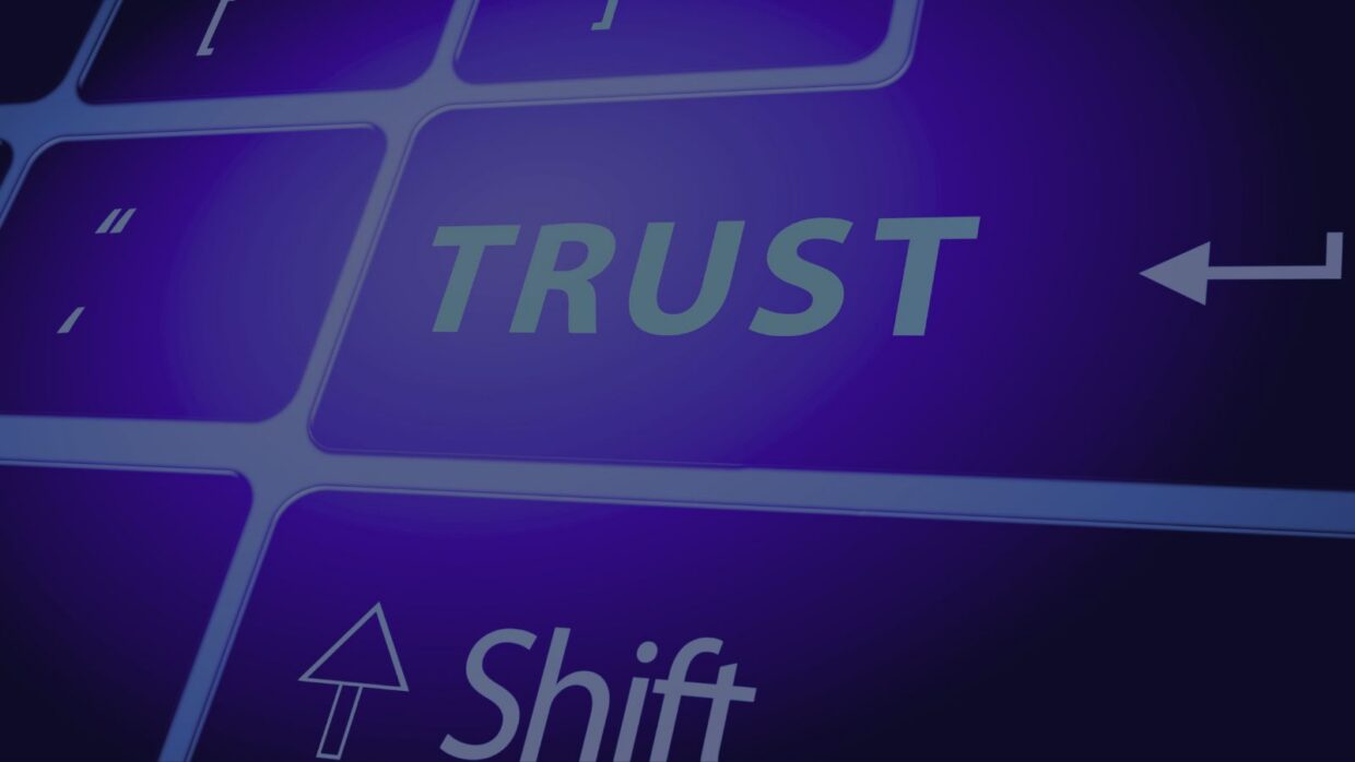 A close-up view of a keyboard with the word "TRUST" prominently displayed on one key. The background features a gradient of purple tones, emphasizing the key's visibility, relevant to a CIO perspective on cybersecurity.